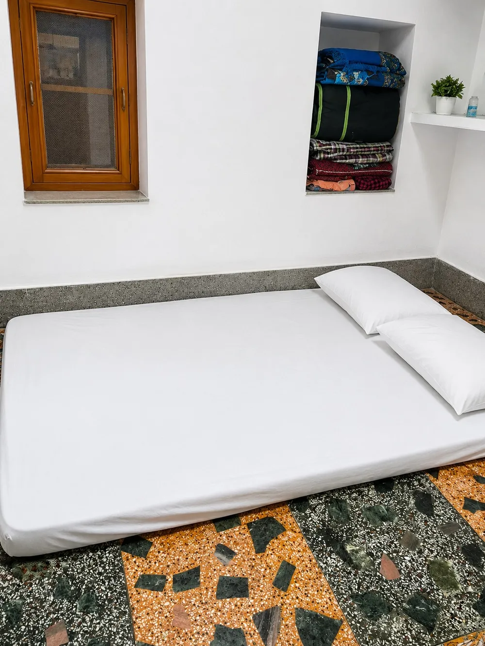 A room at Bharat Bhawan with a mattress made up with white sheets, a window and a niche for bedding